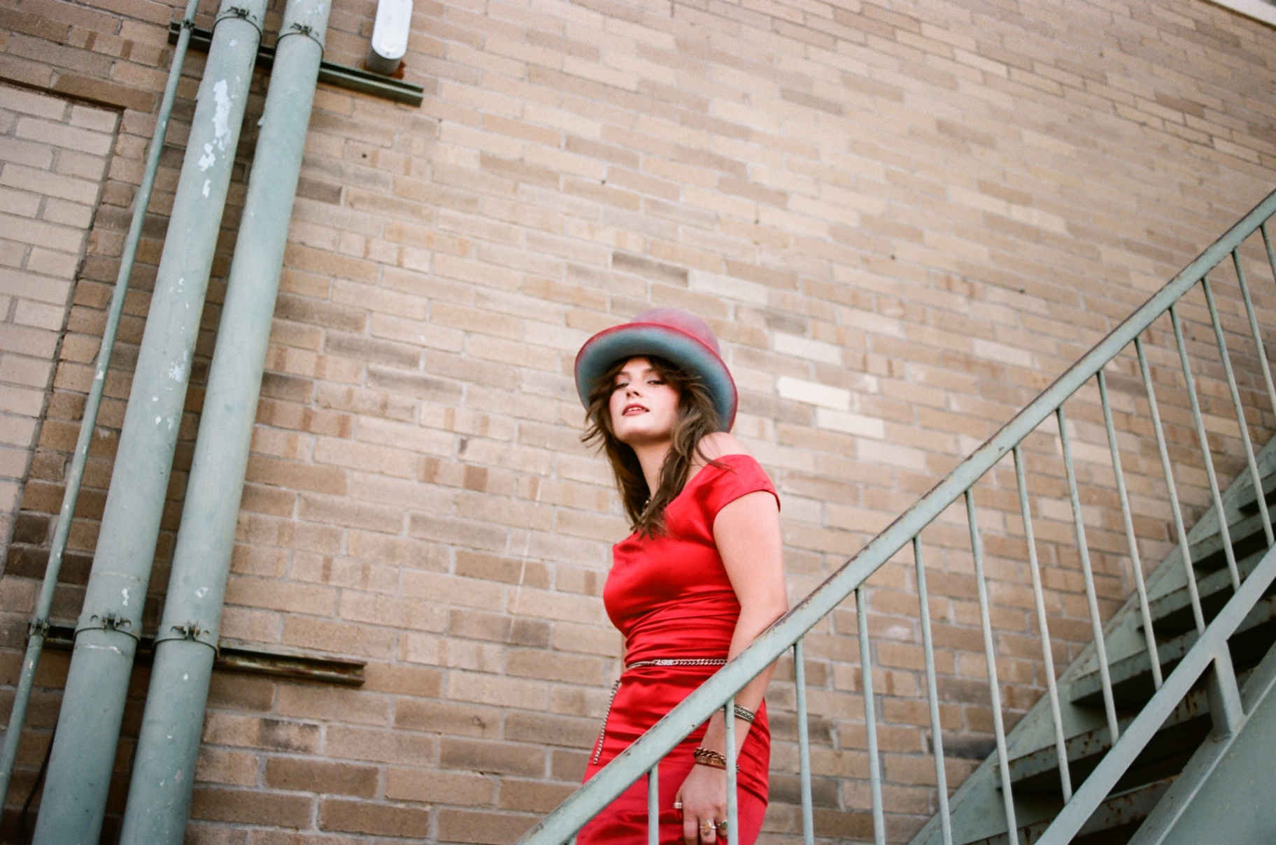 Original 35mm low-angle portrait of a woman in a red dress and hat on a metal staircase