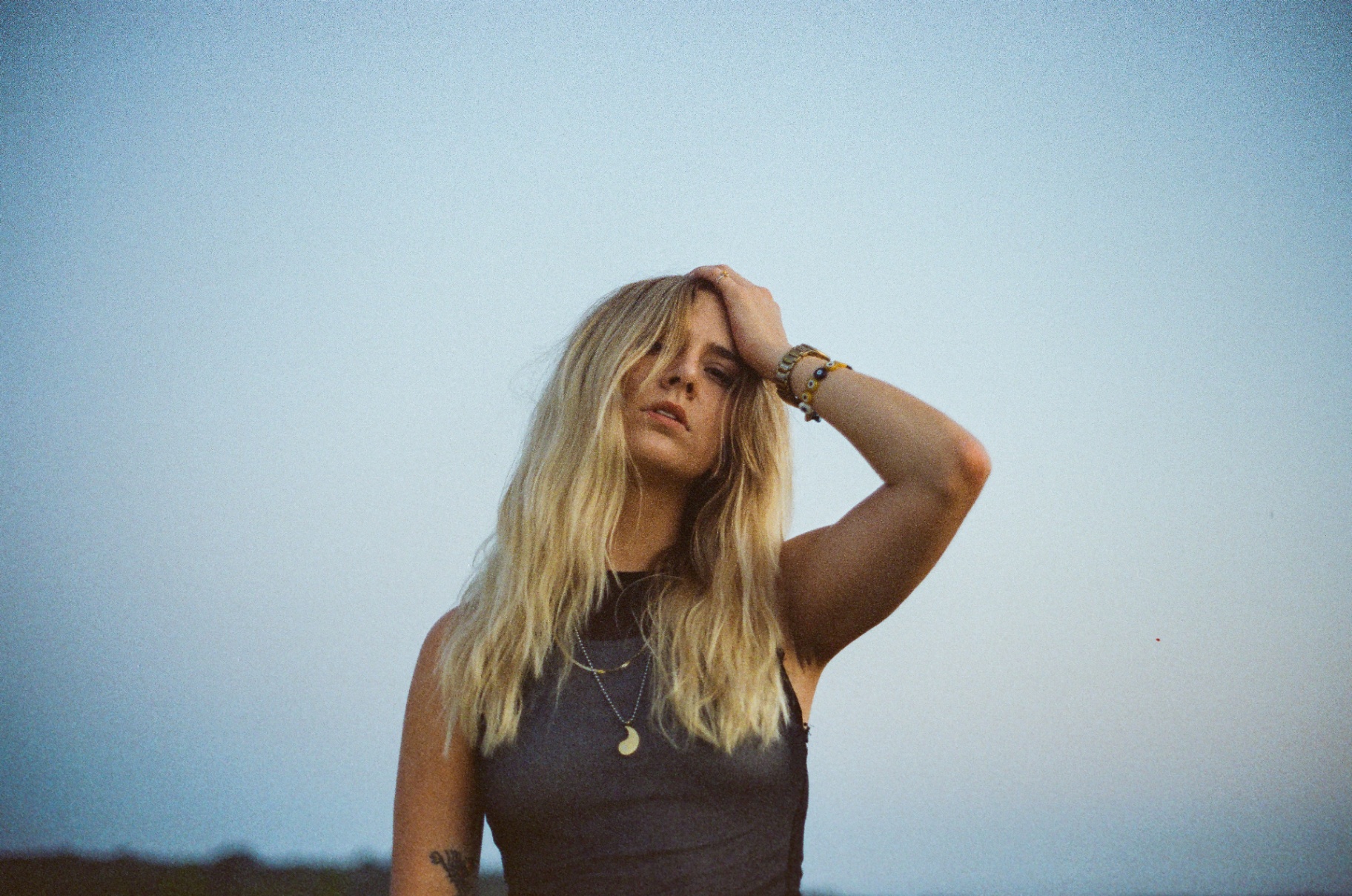 Original 35mm portrait of a blonde woman with her hand in her hair against a pale evening sky