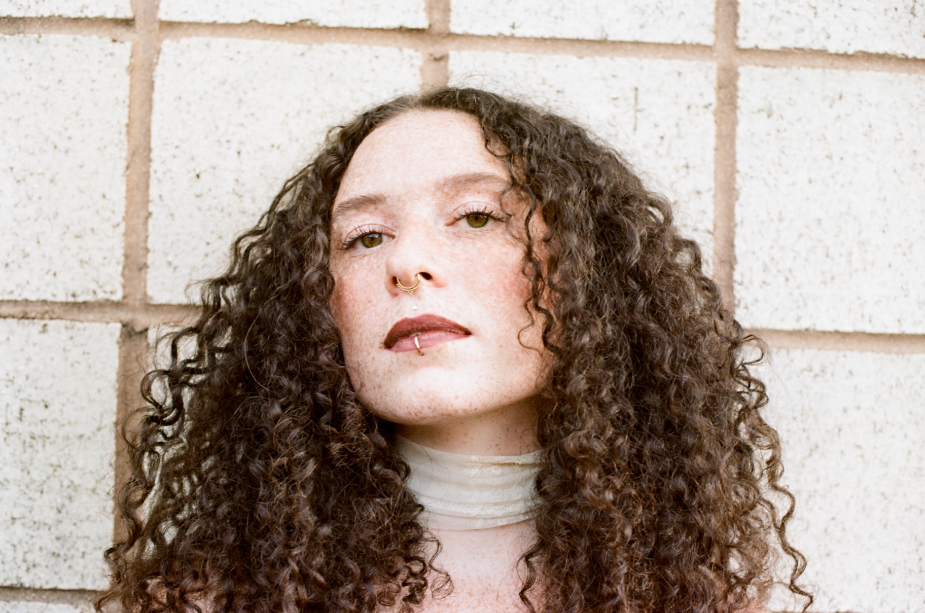 Original close-up 35mm portrait of a woman with curly hair against a white brick wall
