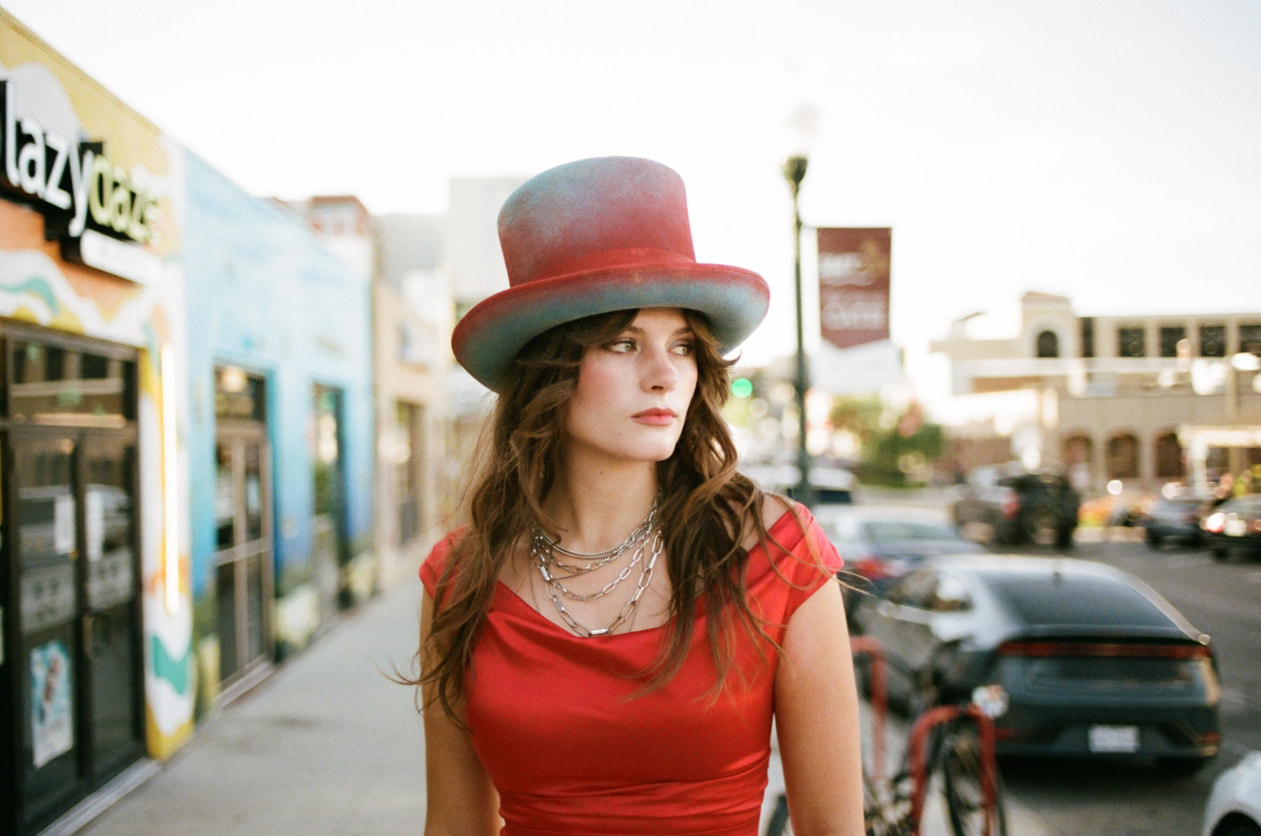 Original 35mm portrait of a woman in a red dress and painted hat walking a storefront sidewalk