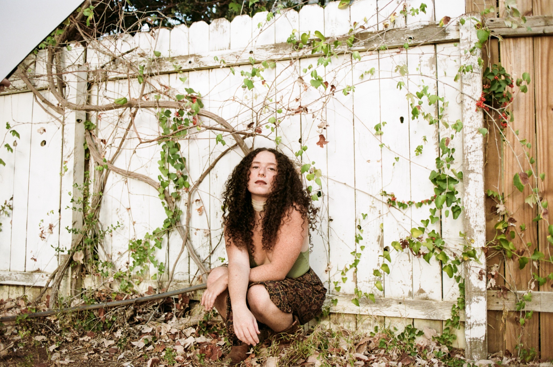Original 35mm portrait of a woman crouched beside a white fence covered in vines